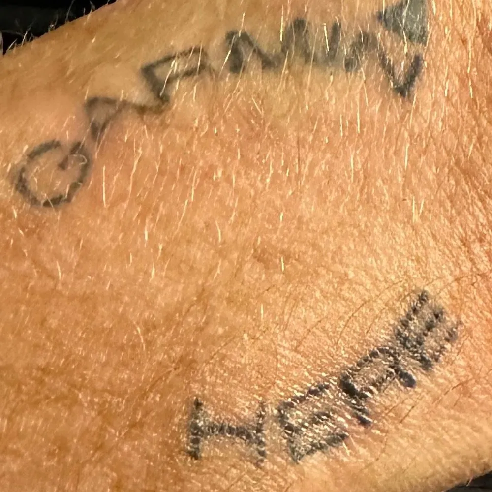 A tattoo on Trevor’s forearm reading GARMIN with an arrow pointing down the wrist, and HERE