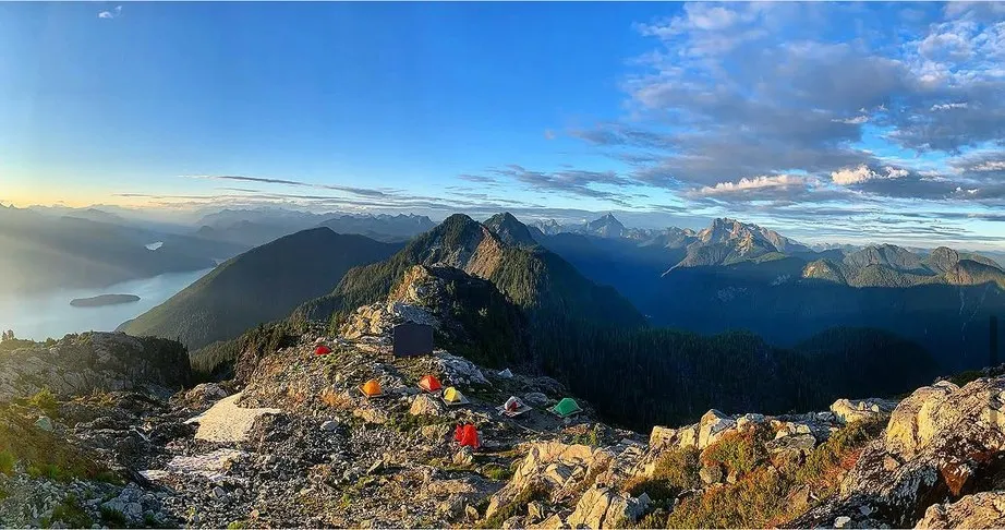 Tents on a rocky ridge above a lake at sunrise, peaks in every direction