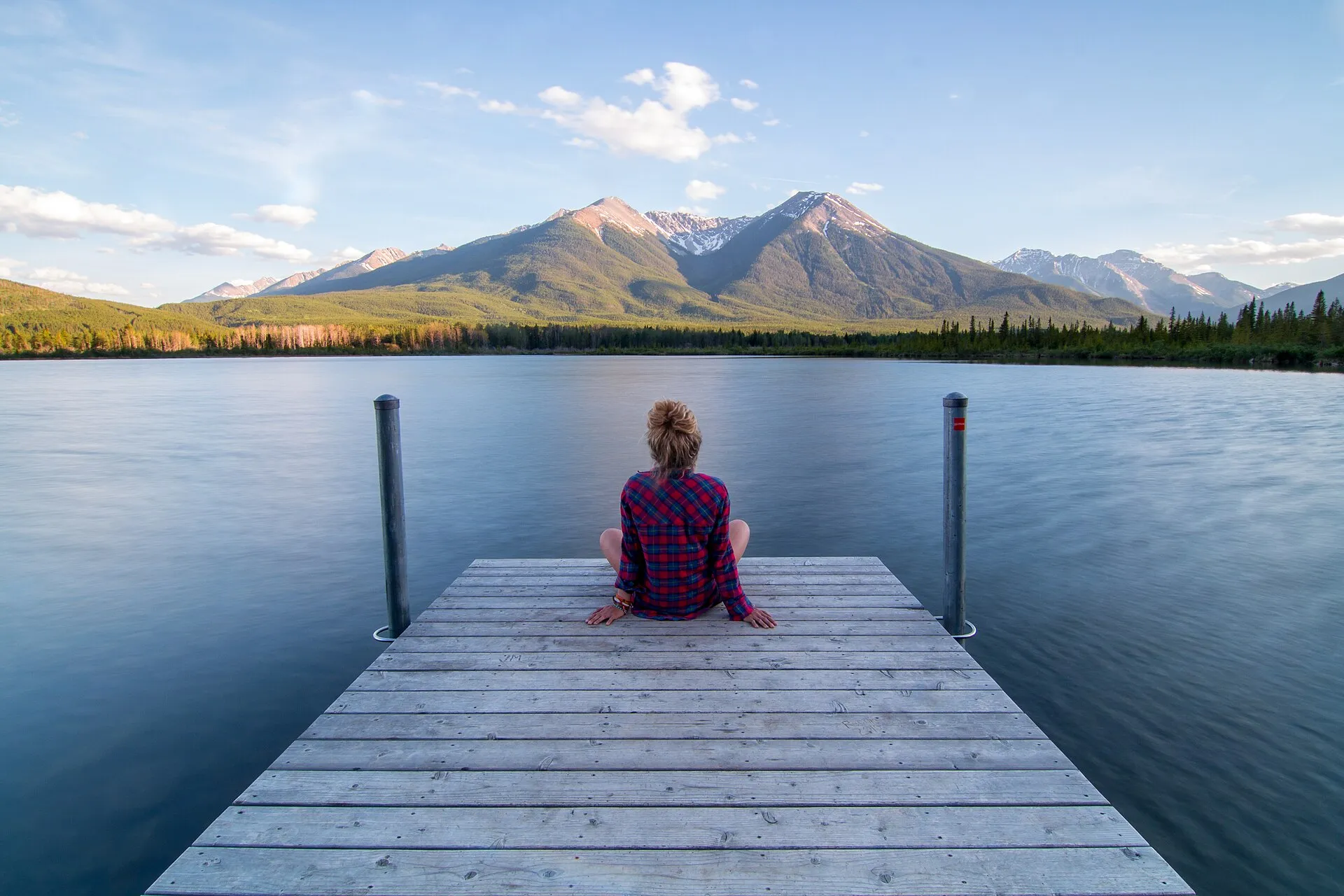 Someone sitting at the end of a dock on Vermilion Lakes, Banff National Park, mountains across the water